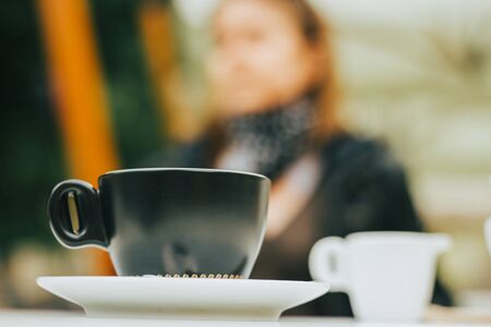 Small green coffee cup on a white plate and milk with a person in background â Stylish ceramic mug for serving hot beverages â Tasty and sweet drink in the morningの写真素材
