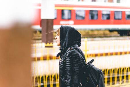 Young woman wearing a leather jacket with a grey hood in a station on a rainy day â Casually dressed girl looking for directions or waiting for the trainの写真素材