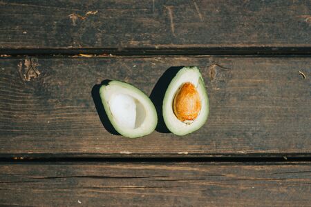 Top view of a single avocado cut in half with brown seed on dark wooden planks â€“ Health...