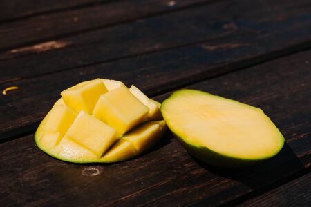 Two slices of a ripe mango one with cubes placed on a wooden surface during day time â Bright yellow exotic juicy fruit on brown background â Healthy and delicious snackの写真素材