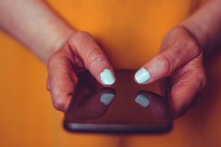 Closeup of a senior womanâs hands holding a black phone â Elderly female with withe nail polish texting on a smartphone â Concept image for old persons using and trying new gadgets and technologyの写真素材
