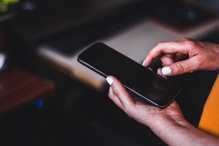 Elderly woman hands holding a big black smartphone indoor â Senior lady wearing an orange blouse and with white nail polish using a mobile phone â Concept image for old people and technologyの写真素材