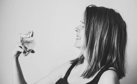 Smiling young woman spraying perfume on her neck on a white background â Happy girl trying delicate scent of fragrance â Concept image for eleganceの写真素材