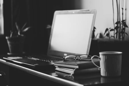 Laptop, notebooks and a pair of reading glasses sitting on a desk with green plant in background â Small working place with portable device at home - Concept image for home office and freelancingの写真素材