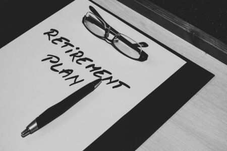 Sheet of paper with the message retirement plan handwritten on it, a pair of reading glasses and a pen placed on a clipboard â Concept image for money planning, and thinning about the futureの写真素材