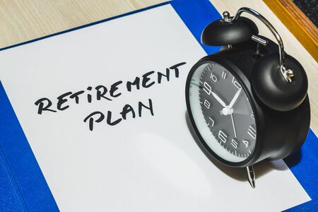 White sheet of paper with the message retirement plan written on it and a retro black alarm clock on...