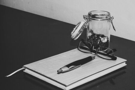Jar with coins, a pair of reading glasses a pen and a white empty sheet of paper sitting on a clipboard on a desk â Concept image for financial education and money planningの写真素材