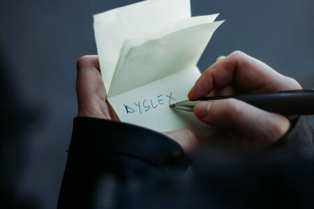 Closeup of a young personâs hands writing the word dyslexia on a yellow post it with a black pen â Spelling disability treated with practice and exercise â Concept image for dyslexiaの写真素材