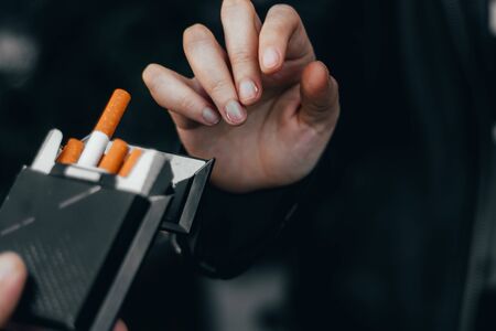 Young personâs hand reaching for an open pack of cigarettes â Toxic habit that causes cancer and heavy addiction â Concept image for negative temptation and no smoking dayの写真素材