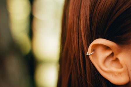 Closeup of a young womanâs pierced ear with a silver ring with a small ball â Girl with brown hair wearing a special earringの写真素材