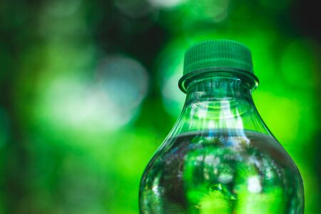 Plastic bottle top full with water with green cap in a park or garden with green trees in blurred background â Recyclable beverage container that protects the natureの写真素材