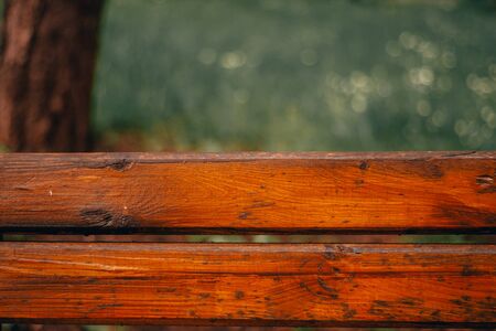 Bright brown old wooden boards from a bench top in the park with green blurry background in the park â Rough and weathered timber surface with small natural cracksの写真素材
