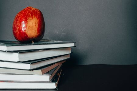 Big red apple sitting on top of a book stack in front of a chalkboard background â Concept image for literature encouragement, reading, back to school and healthy nutritionの写真素材