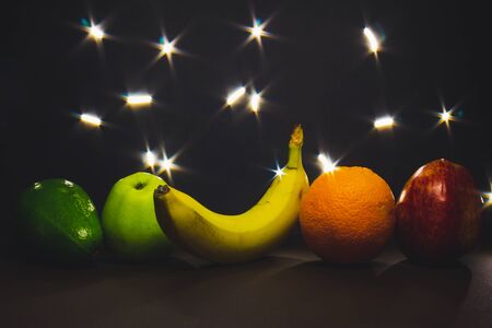 Fruits sitting in a row arranged by with flashing lights in background -Delicious and sweet snacks in a vegetarian diet â Concept image for healthy lifestyleの写真素材