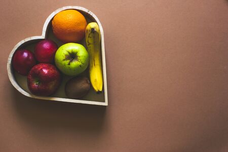 Heart shaped wooden fruit bowl with multiple fruits on a cream background with copy space â Concept image for healthy lifestyle, wellness and diet for blood pressureの写真素材