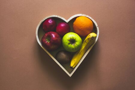 Wooden heart shaped blow with fresh and ripe fruits sitting on a bright brown background with copy space â Concept image for healthy dietの写真素材