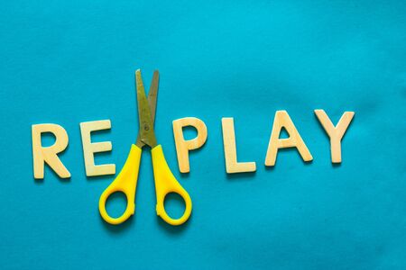The word replay written from wooden letters and a plastic yellow scissor on a bright blue backgroundの写真素材