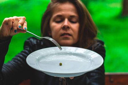 Young woman trying to take one green pea from a wide plate with a fork â Girl eating small quantity of food for weight loss â Tasty nutritious vegetable for a healthy dietの写真素材
