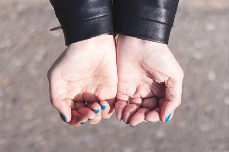 Young woman wearing leather jacket holding her hands in shape of a cup with grey background on a sunny day â Girl doing the giving signの写真素材