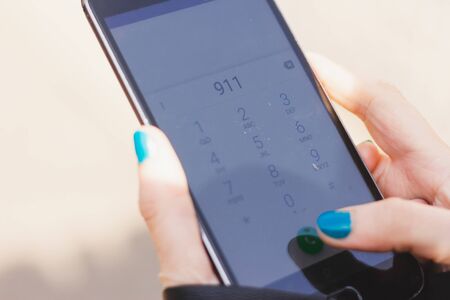 Young woman holding a smartphone while calling 911 â€“ Person dialing emergency service for...