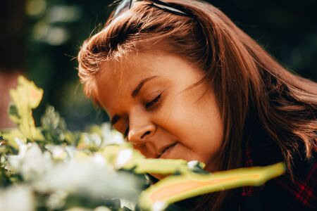 Smiling young woman with brown hair leaning her head over a green bush in the sun â Pretty girl enjoying nature in sunlight while holding her eyes closedの写真素材