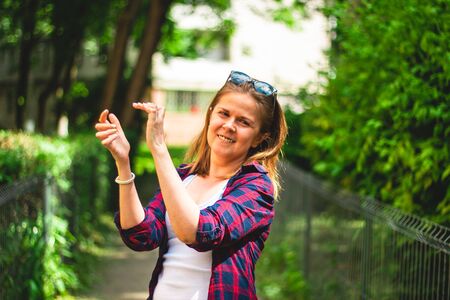 Smiling young woman wearing a plaid shirt clapping her hands with excitement â Casually dressed millennial cheerfully applauding on the streetの写真素材