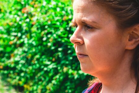Portrait of worried young woman with brown hair in the heat of summer outdoor â Tired girl looking in the distance on a hot day with green backgroundの写真素材