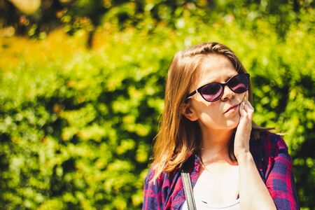 Young woman with short brown Hair holding her hand over her jaw while having a tooth pain â Casually dressed girl experiencing a dental ache in natureの写真素材