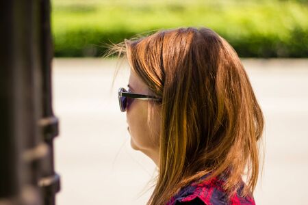 Young woman with short brown hair and a black pair of sunglasses sitting in the bright got sun â Girl enjoying summertime outdoor in the parkの写真素材