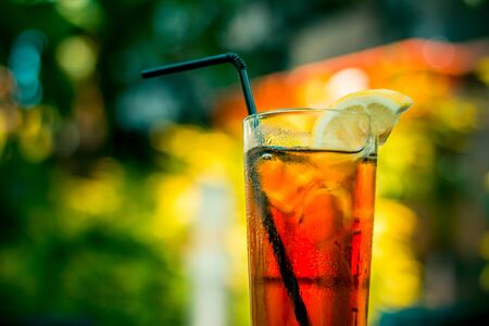 Cold ice tea in a glass with ice cubes and a black straw on a table at the barの写真素材