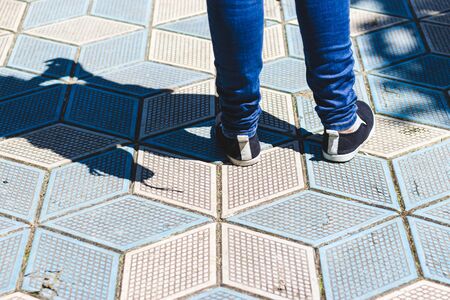 Close-up shot of personâ€™s feet wearing jeans and black shoes standing on a paved sidewalk in...