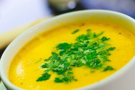 Delicious yellow chicken soup with green parsley on top in a white bowl at the restaurant â Creamy and healthy dish perfect for the main courseの写真素材