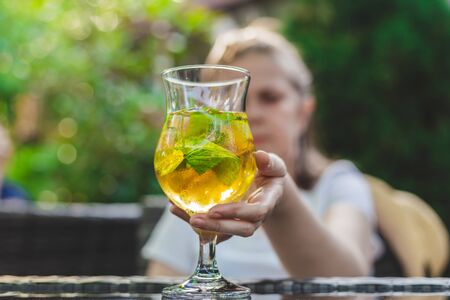 Young woman sitting at a terrace grabbing a glass with ice tea that is placed on the table â€“...