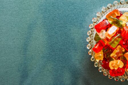 Close-up shot of mixed color gummy bears placed in a small bowl of glass on a grey background â Sweet and tasty treats with fruity flavor with copy spaceの写真素材