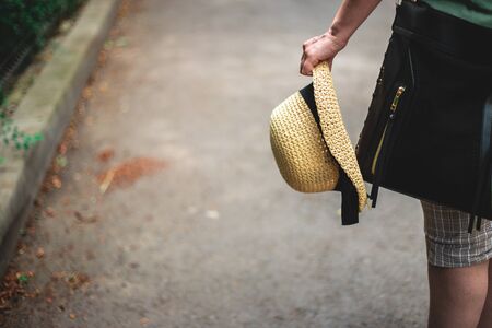Person with black bag holding a straw hat with one hand in the city â Casually dressed young woman with summer hat and purse with copy spaceの写真素材