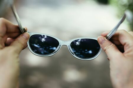 Close-up shot o sf young person holding a pair of stylish black sunglasses outdoor â€“ Woman hand with hipster eye ware on a grey background