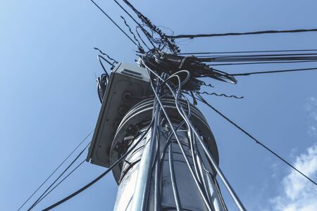 Tangled black communication cables hanging on a tall cement pillar with blue sky in background...