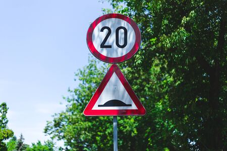 20 kilometers per hour speed limit and bumper road signs in the city on the same pillar â Traffic signs against illegal driving with sky and trees in background with copy spaceの写真素材