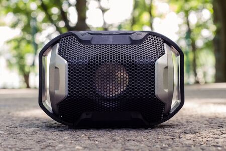 Small plastic portable speaker with black detailed grill placed on ground with blurred background...