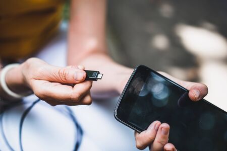 Micro metallic plug for power charging and mobile phone held by young personâ€™s hand outdoor...