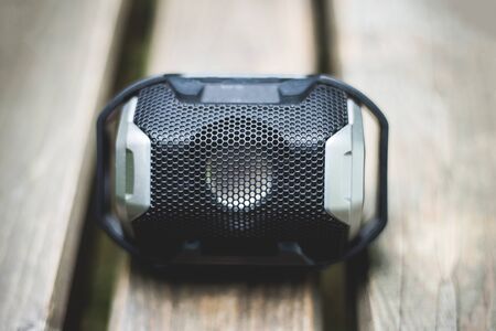 Black portable stereo speaker placed on brown wooden board of a bench in nature â Small wireless modern gadget for playing musicの写真素材