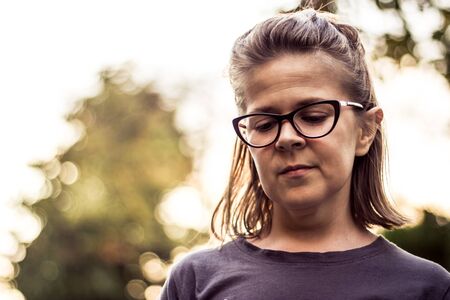 Sad looking girl with glasses looking down in the evening outdoor portrait