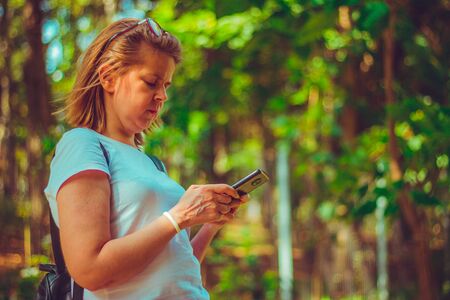 Girl using smartphone in a natural park. Messaging or online chatting while in nature