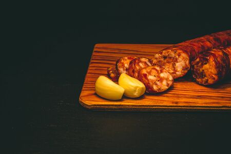Close-up to a raw pork sausage on dark background â Uncooked meat slices next to garlic seeds and a glass bowl of mustardの写真素材