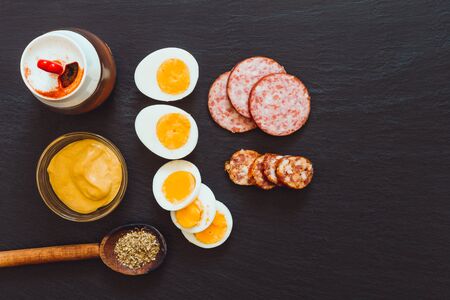 Egg, sausage and salami slices on dark background â Traditional cuisine full of fat and protein on black textured stoneの写真素材