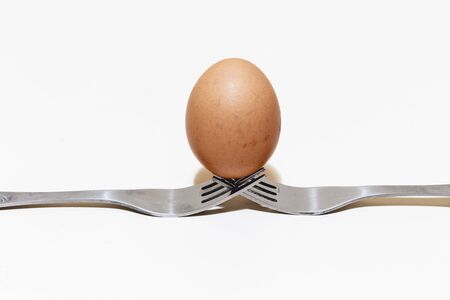 Egg sitting in balance on two silver forks on white background with copy space â€“ Natural and...