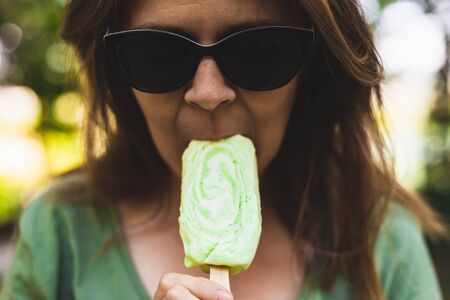 Girl taking a bite from an ice cream â€“ Teenager with sunglasses eating an iced desert in the...