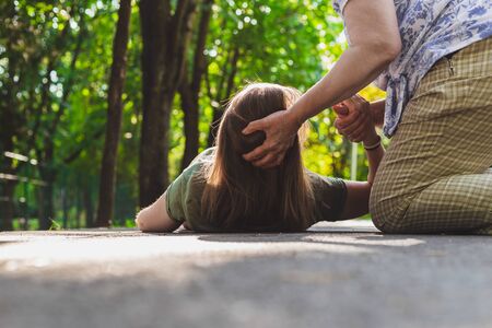 Fainted girl helped by an old woman â Teenager trying to get back on her feet while receiving support from an elderの写真素材