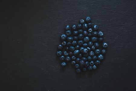 Small fresh berries on black stone textured background - Blueberries as source of vitamins and...