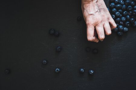 Top view of hand grabbing small blueberries placed on a black background - Healthy and sweet fruits full of vitamins and antioxidantsの写真素材